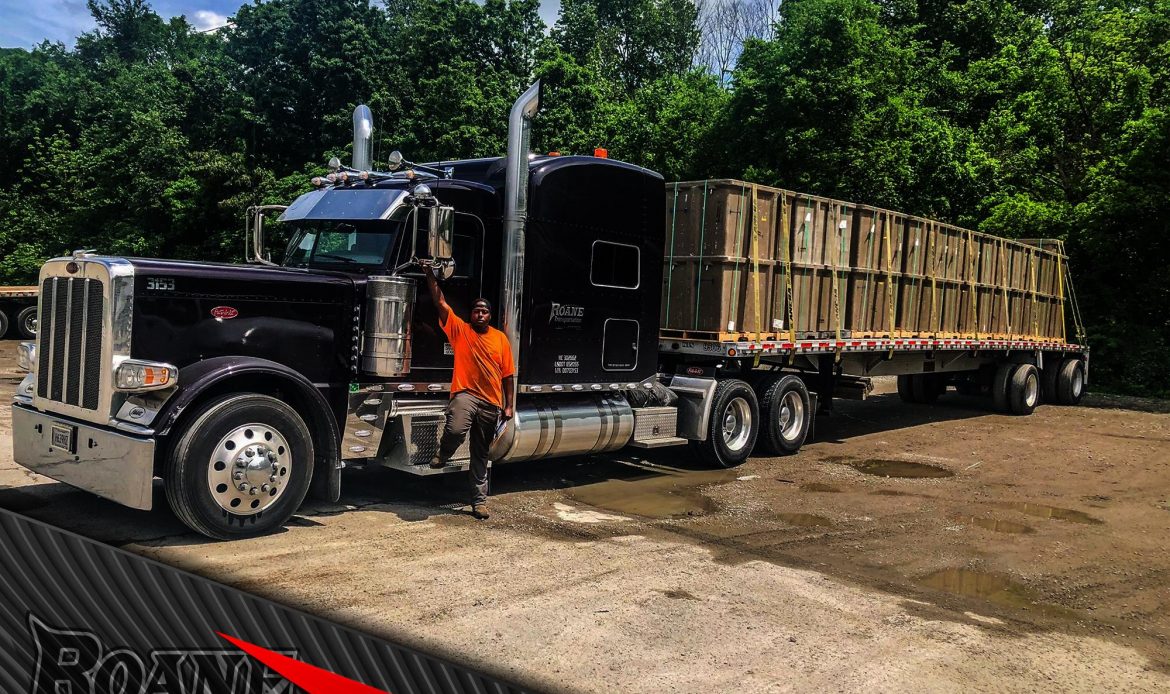 a proud truck driver standing in front of his new peterbilt given to him by roane transportation